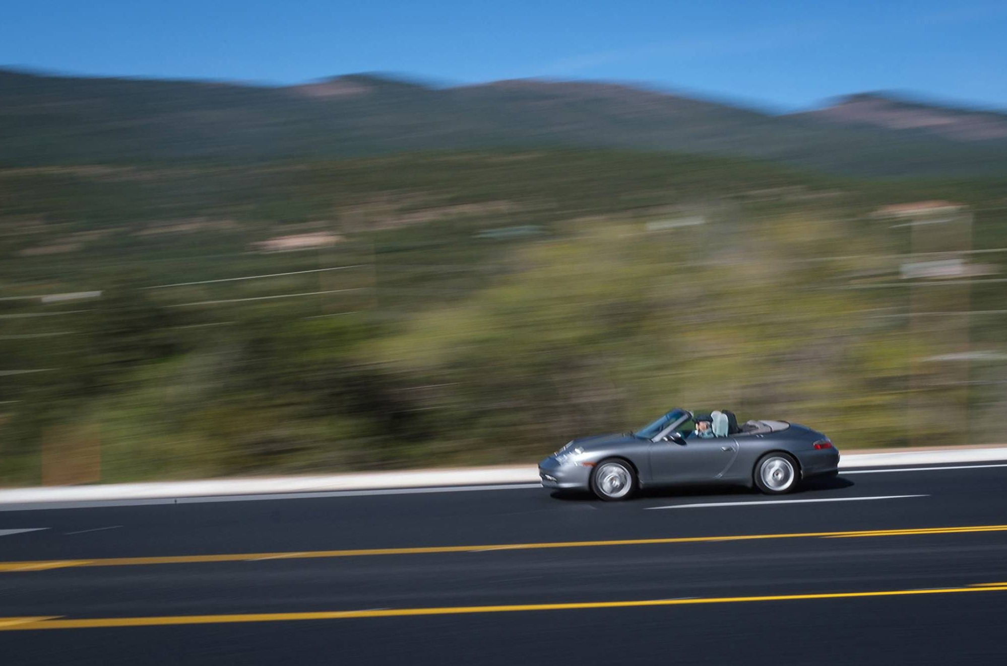 Person in a silver sportscar driving quickly down the highway. The background and foreground are blurred to emphasize the speed of the car