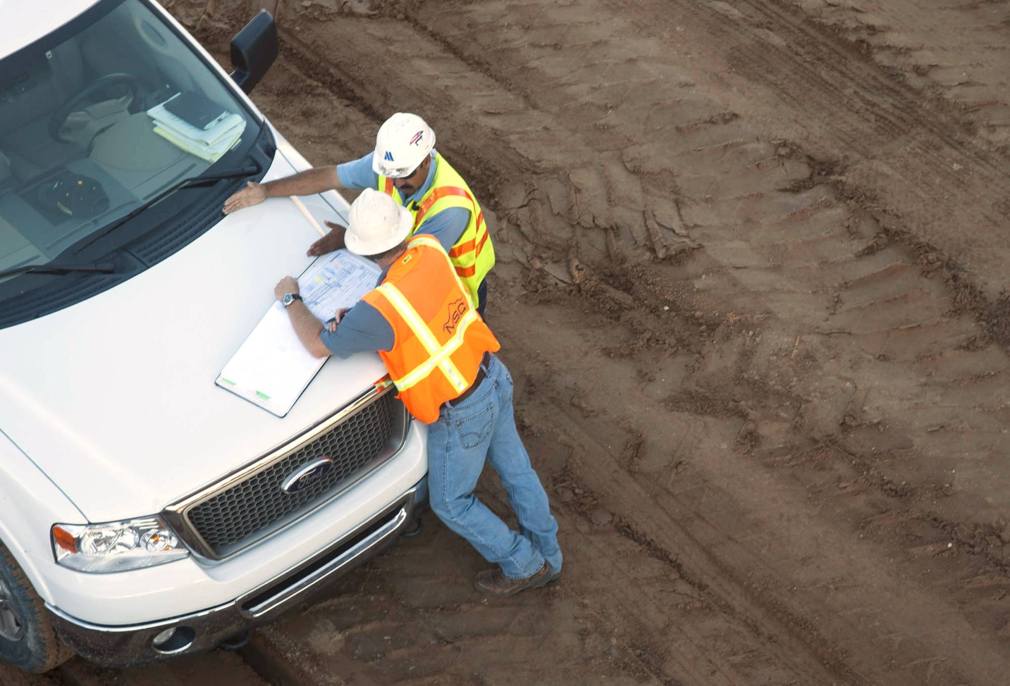 A photo of two men leaning on a truck reviewing a document