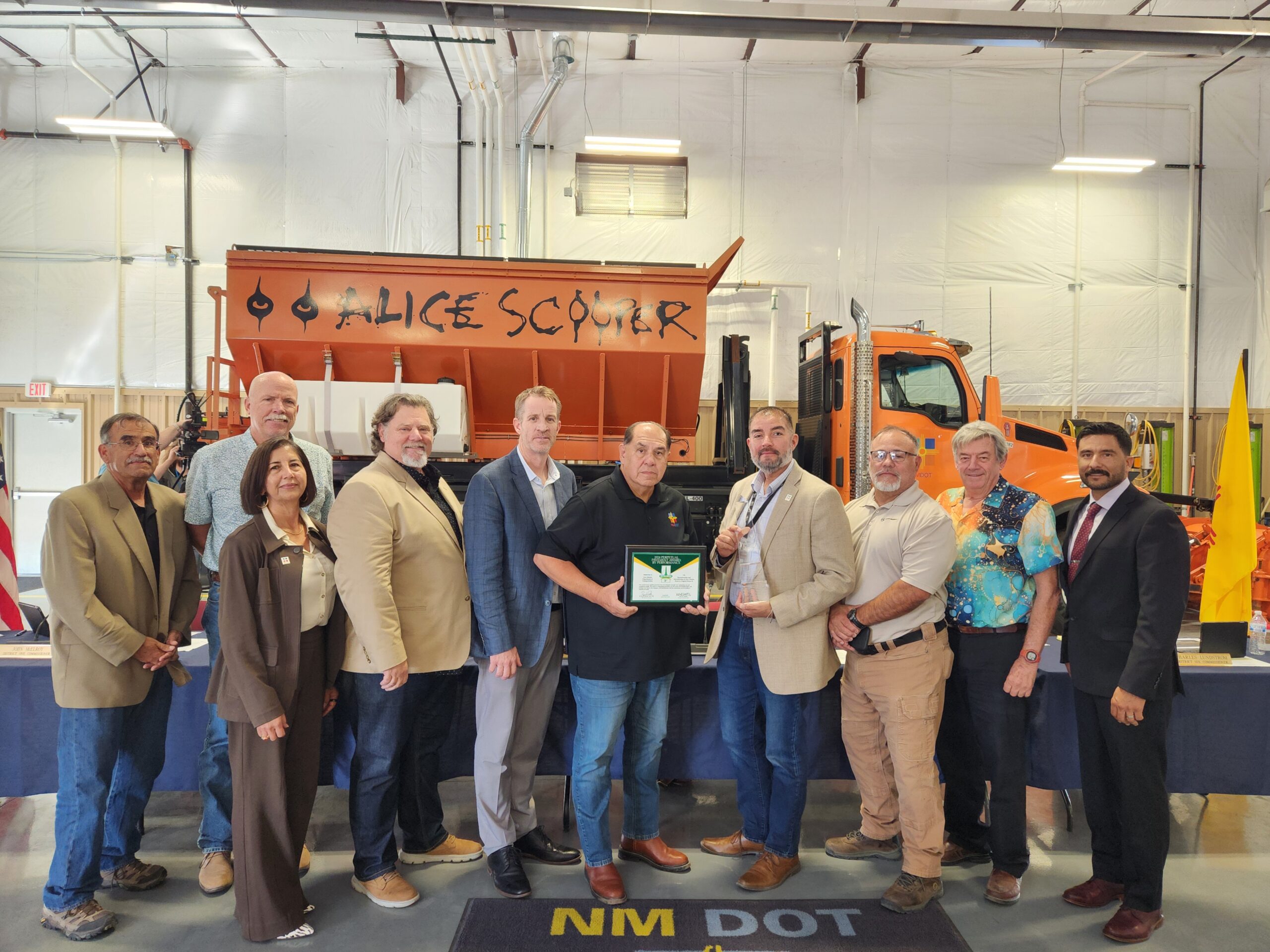 State transportation commissioners and partners posing with national award for excellence on route 66 in front of a snowplow truck