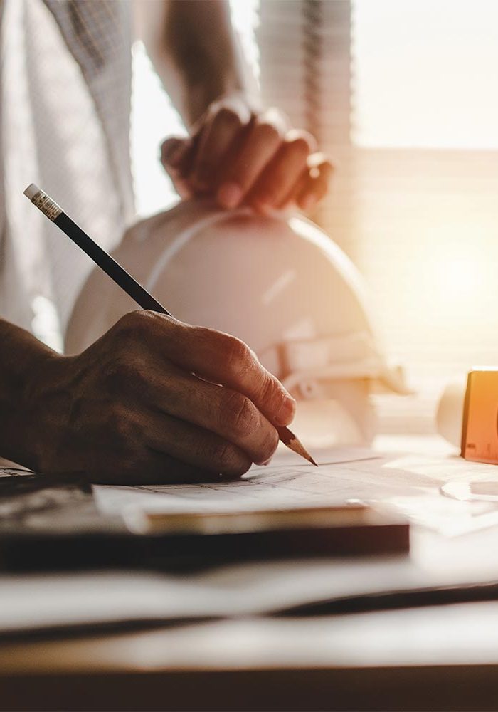 hand on a construction helmet while other hand draws construction plans